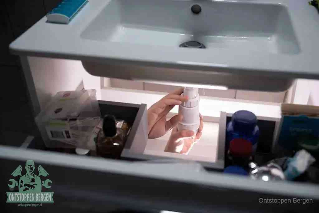 Een pompfles met zeep boven een wastafel, de heet water en afwasmiddel-methode om een vetprop in de afvoer los te maken in Bergen