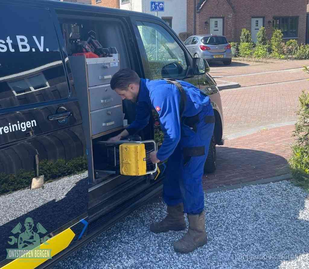 Een monteur pakt buiten op de oprit gereedschap uit de bedrijfsbus, het moment om een professional in te schakelen voor een verstopte afvoer in Bergen