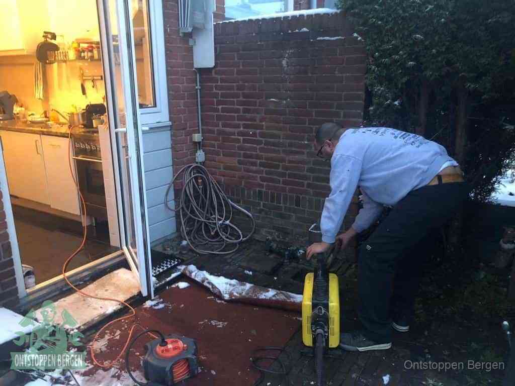 Een monteur werkt buiten bij een open riool-/grondput met een elektrische ontstoppingsmachine om een verborgen afvoerprobleem op te sporen in Bergen