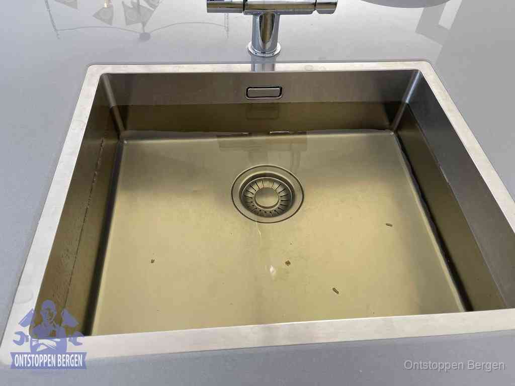Stilstaand water in een rvs spoelbak dat niet wegloopt, een duidelijk signaal van een gootsteenverstopping in Bergen