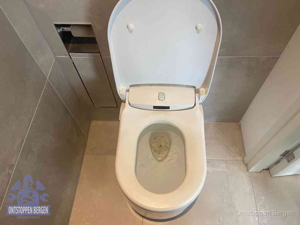 Een wit hangtoilet waarin een prop wc-papier op het water blijft drijven, een duidelijk signaal van een verstopte wc in Bergen