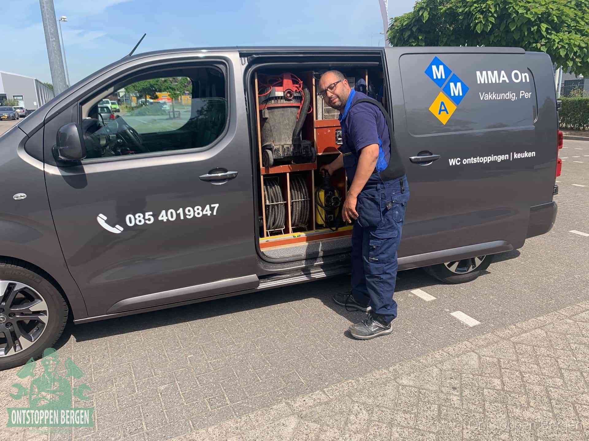 Een monteur bij de open schuifdeur van zijn bedrijfsbus op een parkeerplaats, klaar om de oorzaak van terugkerende afvoerverstoppingen aan te pakken in Bergen