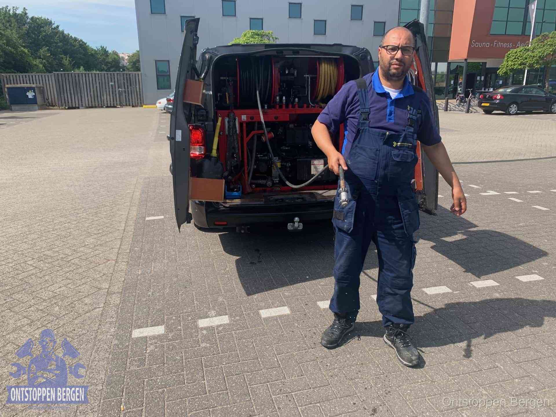 Een monteur bij zijn bestelbus met een hogedruk- en rioolreinigingsunit, klaar om de oorzaak van terugkerende wc-verstoppingen aan te pakken in Bergen
