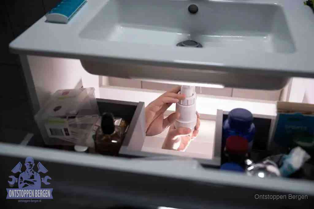 Een pompfles met zeep boven een wastafel in de toiletruimte, de warm water en afwasmiddel-methode om de wc te ontstoppen in Bergen