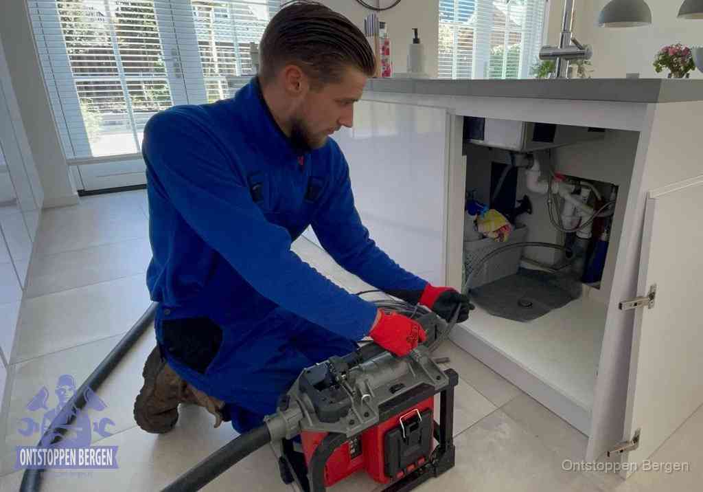 Een monteur voert een professionele elektrische ontstoppingsmachine in de afvoer onder de spoelbak tijdens het gootsteen ontstoppen in Bergen